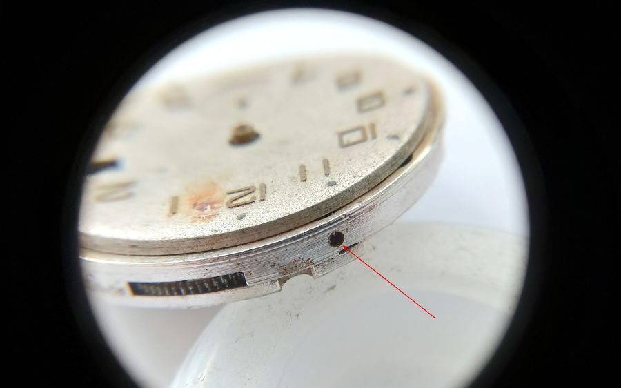 Vostok 2605 movement edge through loupe showing dial foot screw position with red arrow