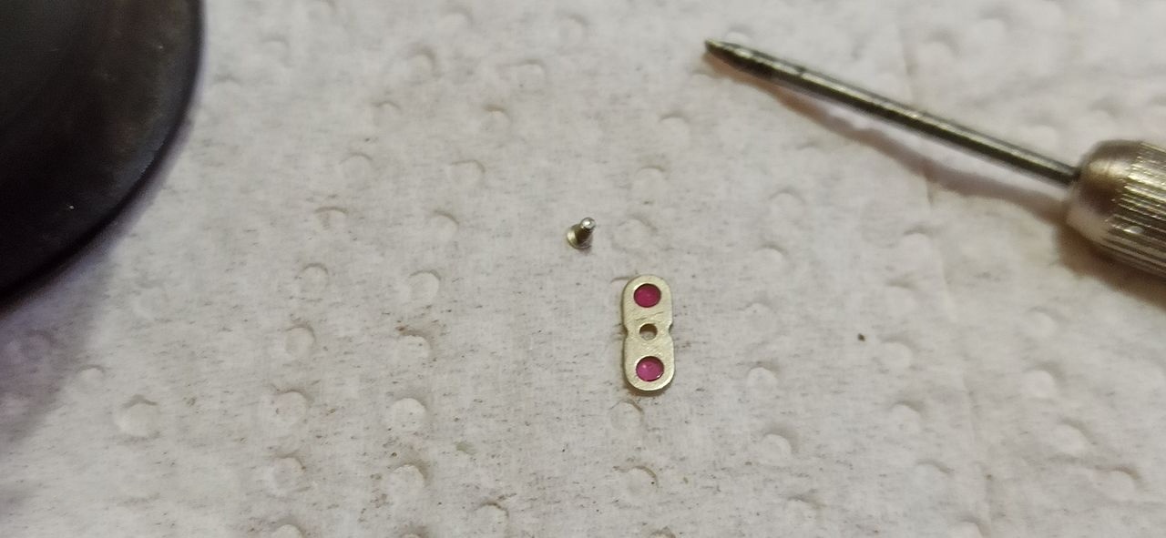 A cap jewel in its setting handled with tweezers on a work cloth
