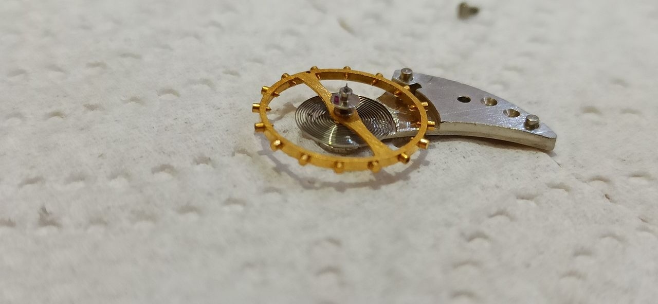 Removed balance wheel and cock lying on a work cloth, showing the large gilt balance