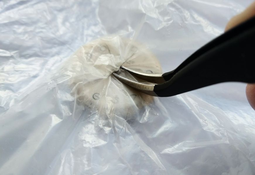 Tweezers lifting the hands through the protective film covering the dial