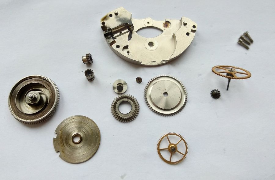 Motor components laid out: center and intermediate wheels, crown wheel, barrel wheel, clutch parts, and mainspring