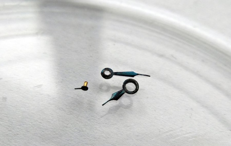 Corroded watch hands in storage dish